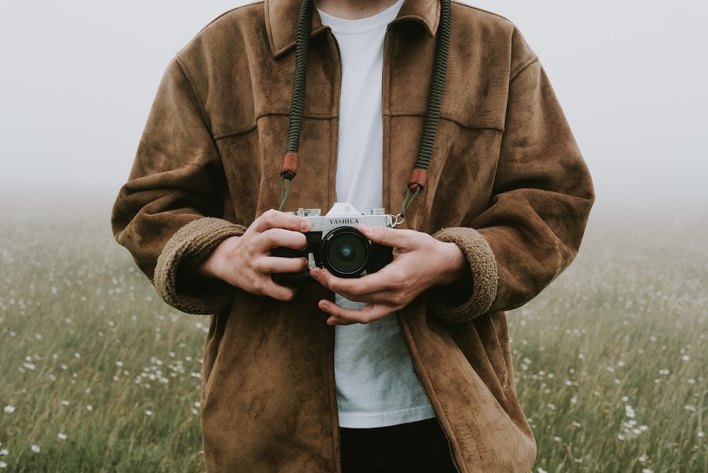 Man holding a digital camera wearing a brown jacket